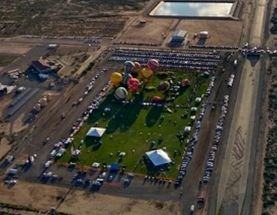 Aerial view of Ed Brabson Balloon Park, green and full of hot-air balloons, surrounded by desert